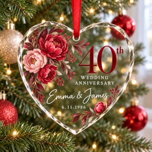 Op de afbeelding: Een hartvormig, transparant acryl ornament met een rood lint. Het ontwerp bevat donkerrode en roze bloemillustraties, de tekst 40th WEDDING ANNIVERSARY, de namen Emma & James en de datum 6.11.1986 in witte en rode letters.
