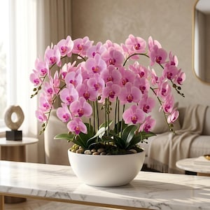 May include: A large arrangement of pink phalaenopsis orchids with multiple stems and vibrant magenta centers, planted in a smooth white ceramic bowl filled with decorative river stones and green foliage, displayed on a white marble surface.