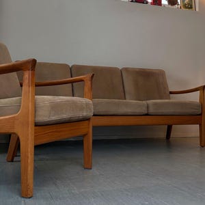 Puede incluir: Un conjunto de muebles de estilo moderno de mediados de siglo, que incluye un sofá y dos sillones. Los marcos de madera tienen un acabado natural y los cojines están tapizados en una tela marrón claro. El diseño es limpio y minimalista.