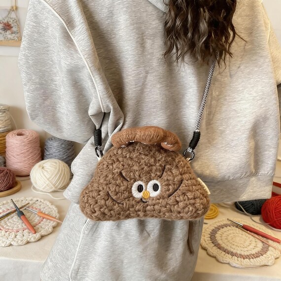 A fully functional mini crossbody purse crocheted in the shape of a poop emoji — handmade craft meets absurdist fashion statement.