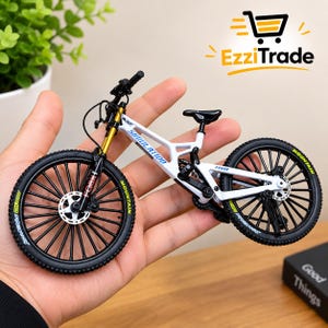 Peut inclure: Un modèle réduit de VTT blanc avec des roues noires, des fourches de suspension avant dorées et un guidon noir. Le cadre porte l'inscription SIMULATION et FF510, tandis que les pneus sont marqués MOUNTAIN. Le vélo est équipé de freins à disque.