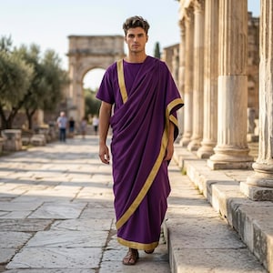 May include: A deep purple toga featuring a gold trim along the edges. The garment is draped over one shoulder, creating a layered effect with short sleeves and a floor-length hem. The fabric is solid in color with a smooth texture and gold borders.