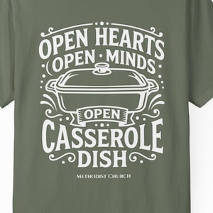 May include: An olive green short-sleeve t-shirt featuring a white graphic print of a rectangular casserole dish. The text reads: OPEN HEARTS OPEN MINDS OPEN CASSEROLE DISH METHODIST CHURCH. The design includes decorative swirls and dots.