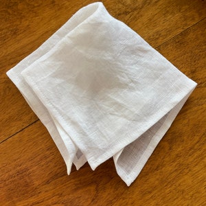May include: A white linen napkin folded into a triangular shape. The napkin is lying on a wooden surface.