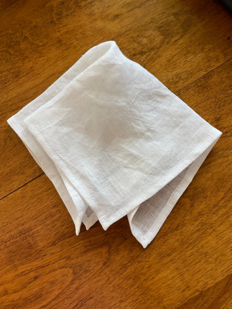 May include: A white linen napkin folded into a triangular shape. The napkin is lying on a wooden surface.
