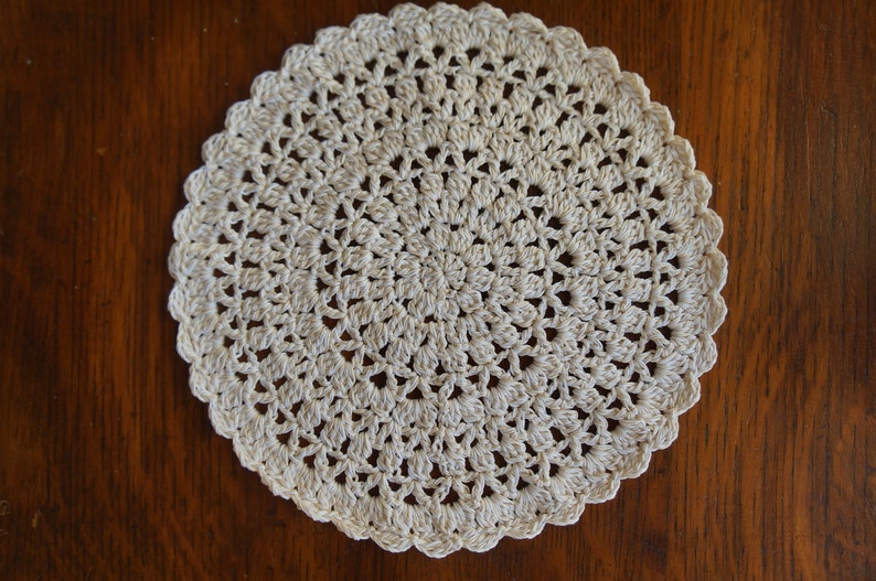 May include: A white crocheted doily with a circular design. The doily is made of delicate, intricate stitches and has a scalloped edge.
