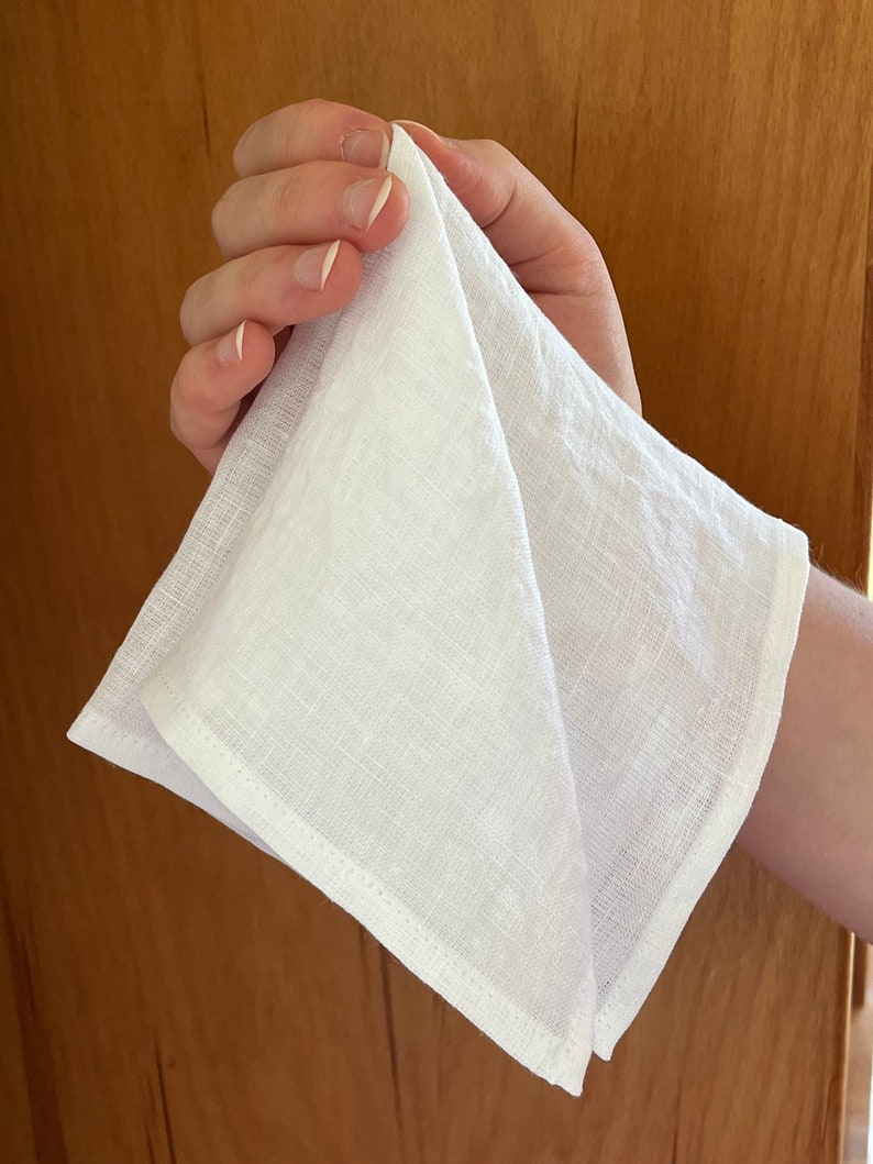 May include: A white linen tea towel folded in half, with a slightly textured surface.