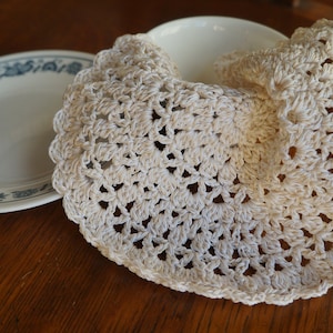 May include: A white crocheted doily with a delicate floral pattern. The doily is folded in half and placed on a wooden table.