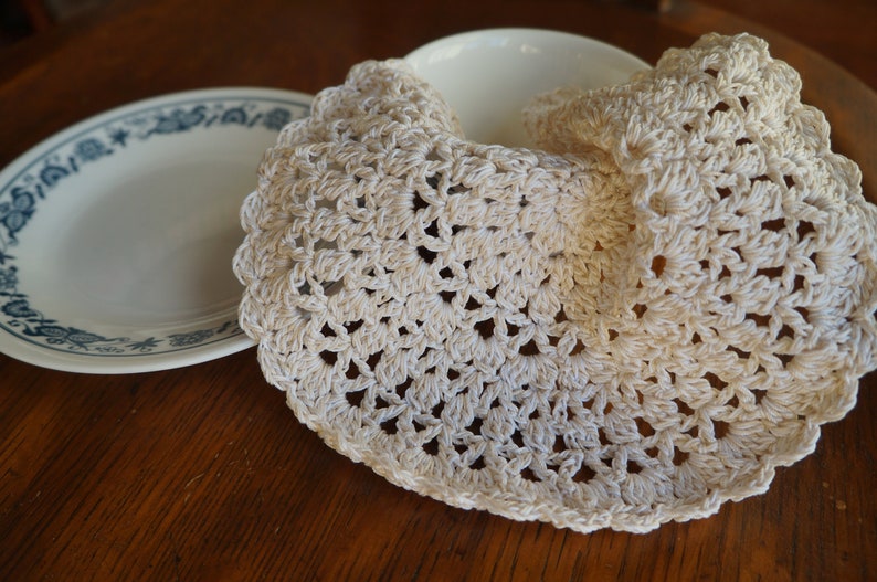 May include: A white crocheted doily with a delicate floral pattern. The doily is folded in half and placed on a wooden table.
