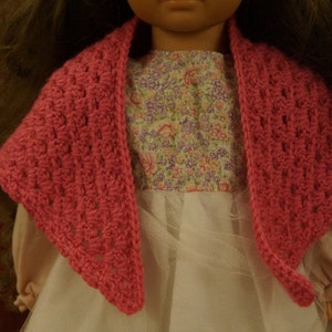 May include: A pink crocheted shawl with a delicate openwork pattern. The shawl is draped over a white dress with a floral print.