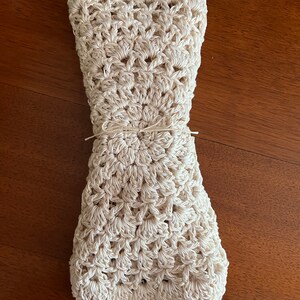 May include: A crocheted cream-colored blanket folded and tied with twine. The blanket has a scalloped edge and a circular pattern in the center.