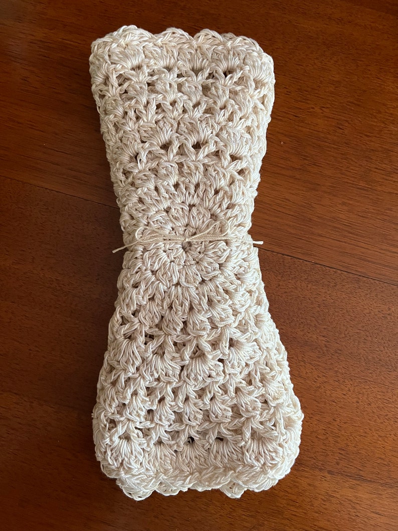 May include: A crocheted cream-colored blanket folded and tied with twine. The blanket has a scalloped edge and a circular pattern in the center.