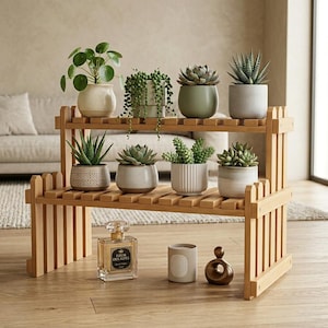 Op de afbeelding: Een houten plantenstandaard met twee niveaus en een hekwerkontwerp met acht potplanten van verschillende soorten. Op de vloer onder de standaard staan een glazen parfumflesje met het label Fleur des Alpes, een cilindrische kaars en een bronzen beeldje.