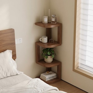 May include: A wooden corner shelf unit with a unique zig-zag design. The shelves hold a small potted plant, books, a mug, candles, and a perfume bottle. The unit is made of dark wood and is placed in a bedroom corner next to a bed.