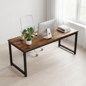 May include: A rectangular desk with a dark brown wood grain surface and a black metal frame. On the desk sits a silver computer monitor, a stack of books, a small white mug, and a potted monstera plant. A white office chair is tucked underneath.