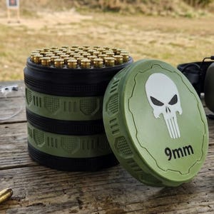 May include: A green and black ammunition container with a skull logo and the text "9mm". The container is open, revealing numerous brass-colored bullets. The lid is off to the side.