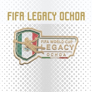 May include: A gold-toned metal pin featuring the text FIFA LEGACY OCHOA. The design includes a shield with the Mexican flag, a silhouette of a goalkeeper in a diving pose, and the text FIFA WORLD CUP LEGACY OCHOA with a small flag accent.