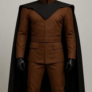 May include: A brown jacket and trousers set featuring a high collar, a matching belt, and two front pockets. A black cape with a V-shaped neckline overlay is worn over the brown jacket. The ensemble includes black gloves and a black head covering.