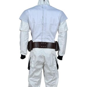 May include: A white jumpsuit with a high collar and a brown belt with pouches. The suit has a quilted design on the shoulders and a zipper down the front. Black cuffs are visible at the wrists and ankles. The overall design suggests a futuristic or military theme.