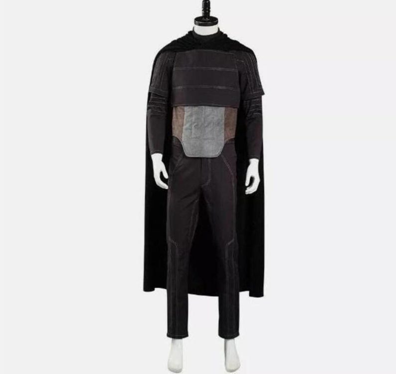 Pode incluir: Um conjunto de fantasia preto composto por uma capa longa, uma blusa de manga comprida com costuras horizontais e um painel central cinzento retangular no peito. O traje inclui cal&ccedil;as pretas a combinar com detalhes de costura subtis.