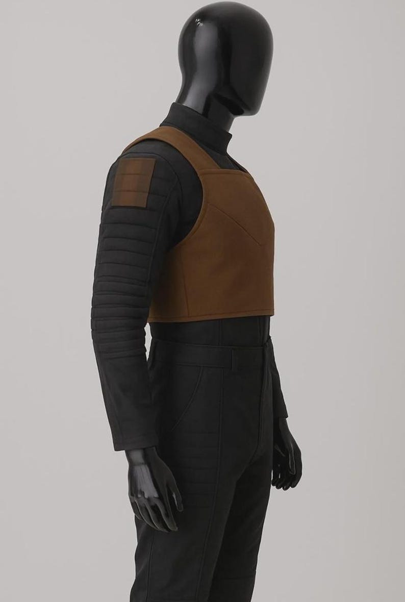 May include: A black long-sleeved shirt with a high neck and horizontal quilted detailing on the sleeves, worn under a cropped brown vest. The vest features a square neckline and a structured, solid design, paired with black trousers on a mannequin.