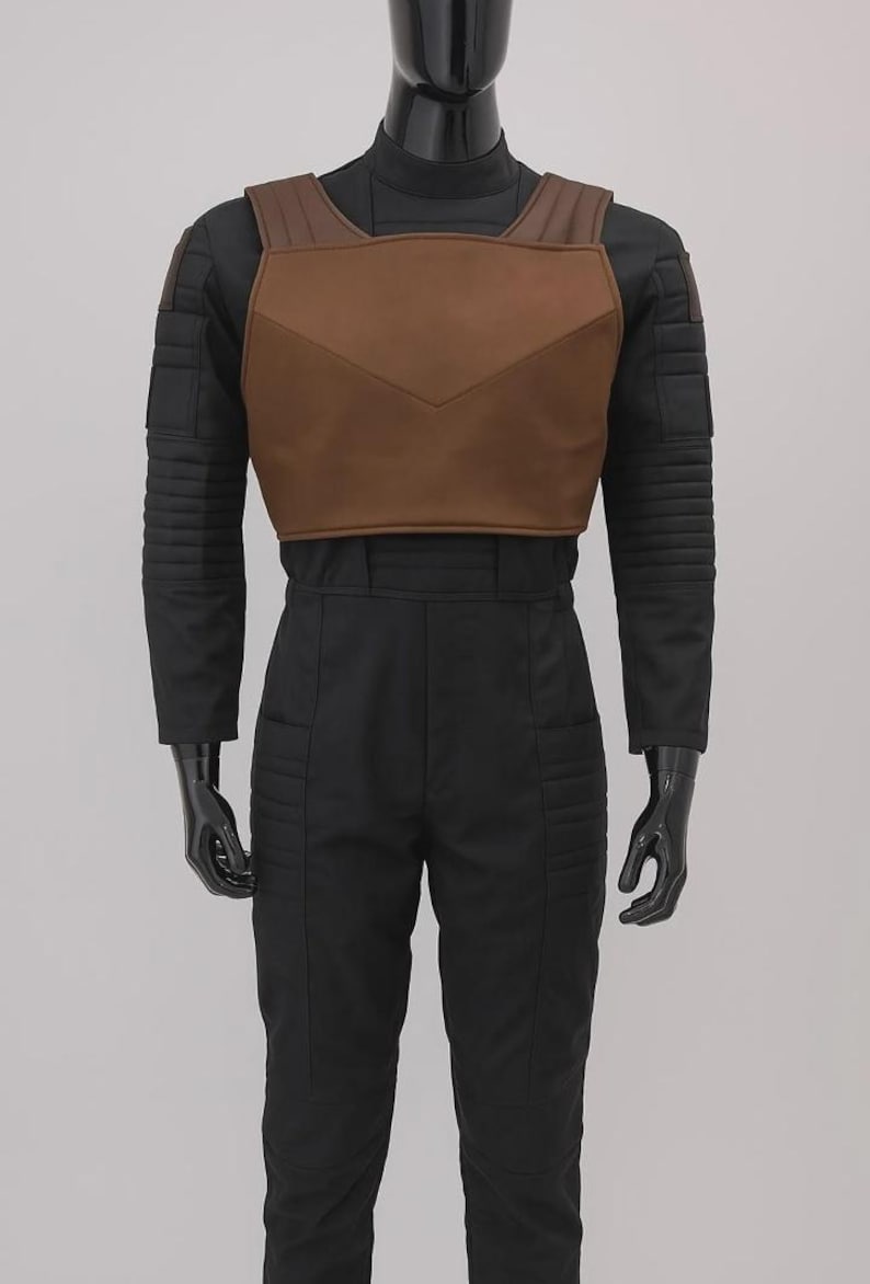May include: A black long-sleeved jumpsuit featuring a high neck and ribbed detailing on the shoulders and thighs. Over the chest is a brown, structured, V-shaped vest piece with wide shoulder straps, worn on a glossy black mannequin torso.
