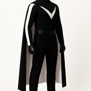 May include: A black jumpsuit featuring a high collar, a white V-shaped chest emblem, and white stripes along the sleeves. The outfit includes a long black cape with a white lining, a black belt, black gloves, and black boots on a mannequin.
