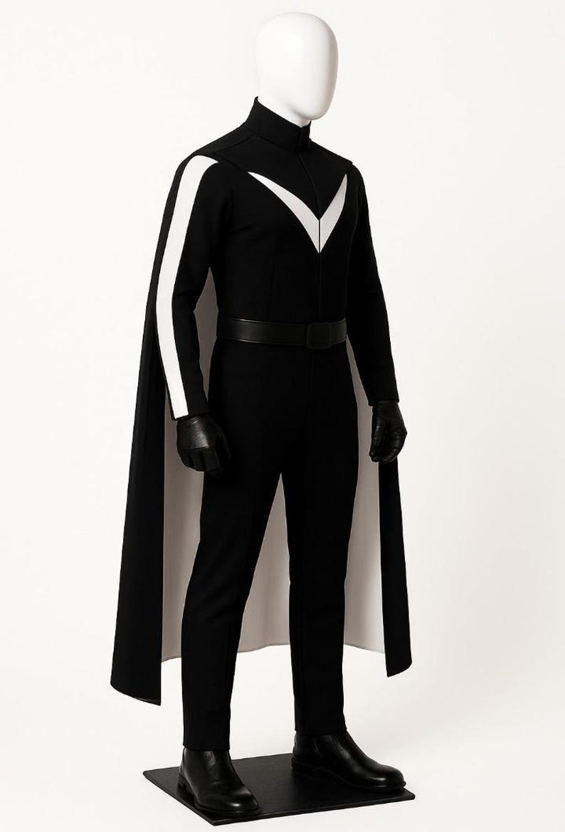 May include: A black jumpsuit featuring a high collar, a white V-shaped chest emblem, and white stripes along the sleeves. The outfit includes a long black cape with a white lining, a black belt, black gloves, and black boots on a mannequin.