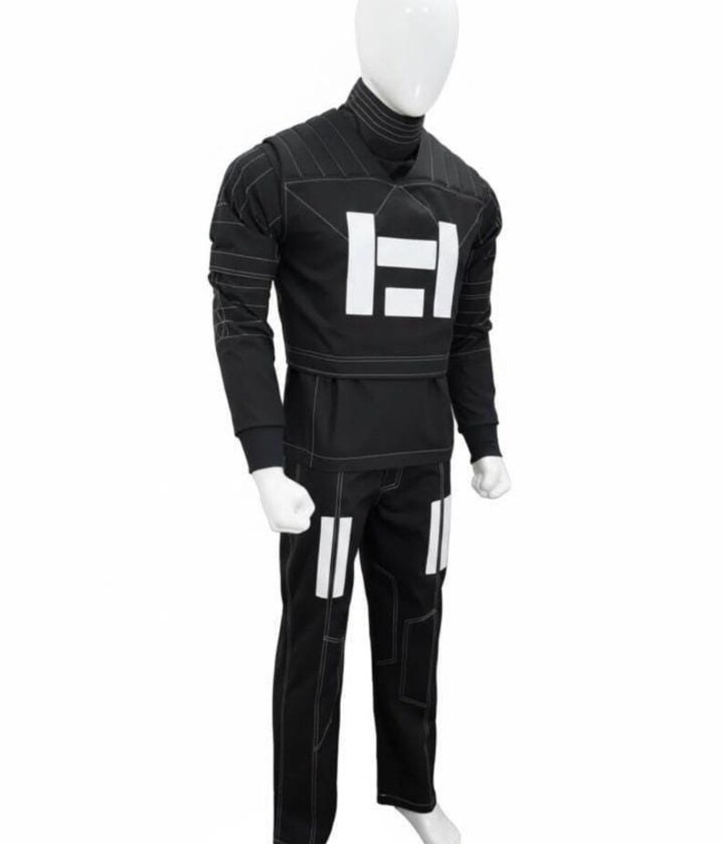 May include: A black long-sleeved shirt and matching pants set featuring white geometric block accents on the chest and thighs. The garment includes a high mock neck collar and prominent white contrast stitching throughout the fabric design.