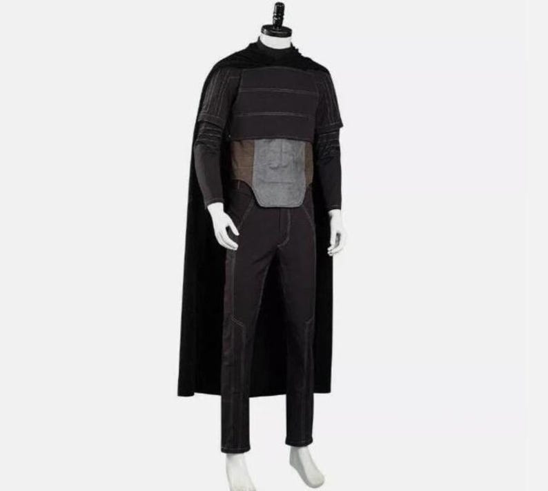 Pode incluir: Um conjunto de fantasia preto composto por uma capa longa, uma blusa de manga curta com costuras horizontais, uma placa abdominal cinza e cal&ccedil;as pretas a condizer com costuras vis&iacute;veis. O conjunto &eacute; exibido num manequim branco.