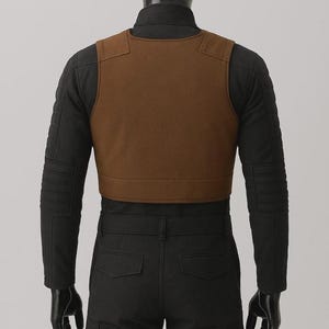 May include: A brown sleeveless vest worn over a black long-sleeved shirt with quilted sleeve detailing and black trousers. The vest features a simple round neckline and a solid, smooth texture, layered over a dark, fitted base garment.