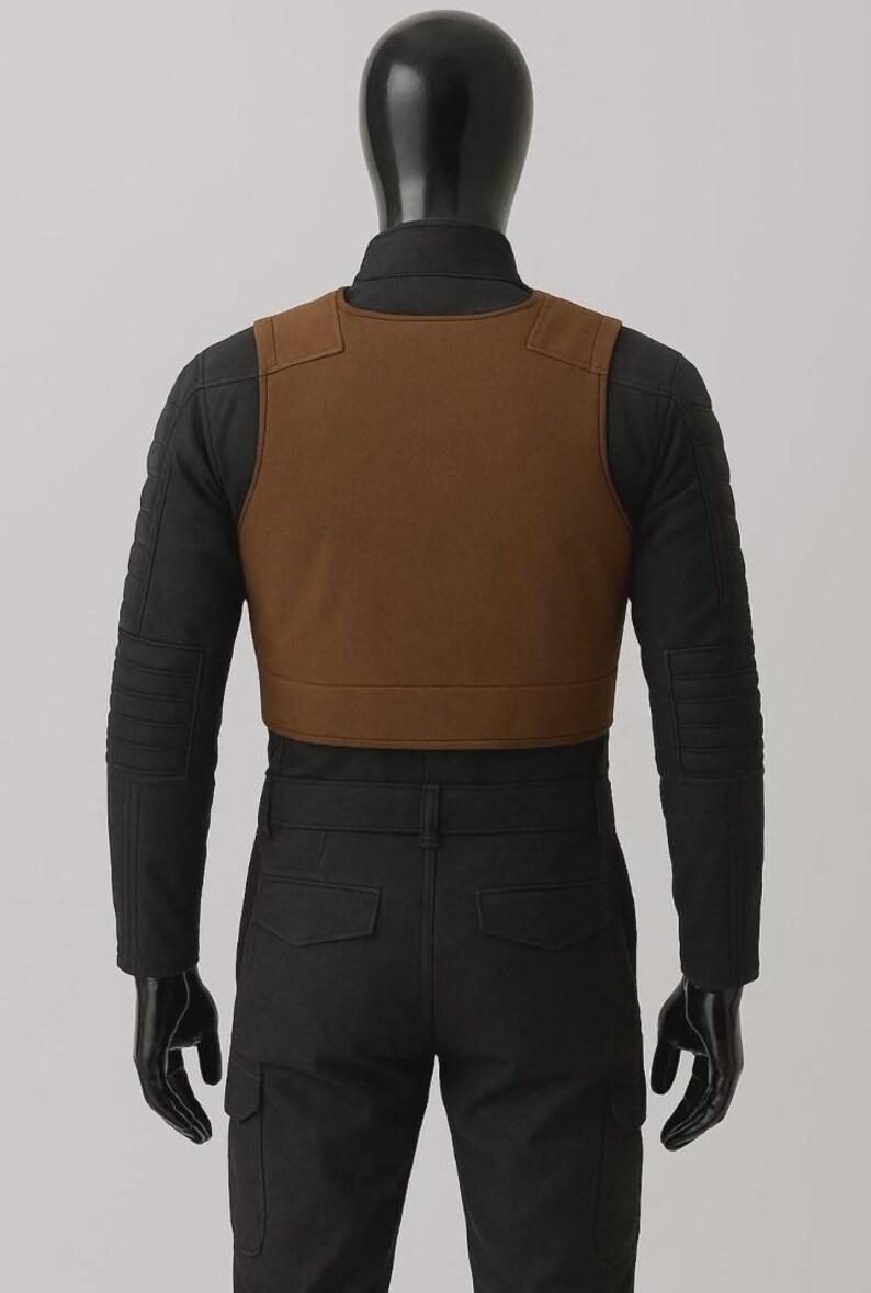 May include: A brown sleeveless vest worn over a black long-sleeved shirt with quilted sleeve detailing and black trousers. The vest features a simple round neckline and a solid, smooth texture, layered over a dark, fitted base garment.