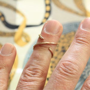 Peut inclure: Une bague dorée avec un design en spirale, portée au doigt. La bague a un style ouvert et minimaliste qui s'enroule autour du doigt. Le design de la bague est simple et élégant, adapté au quotidien.