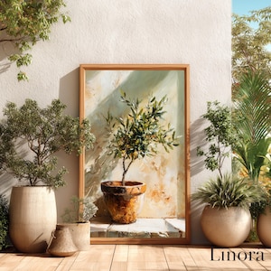 Puede incluir: Una pintura enmarcada de un olivo en maceta, colocada contra una pared de tonos neutros. La pintura está en un marco de madera y está apoyada sobre una superficie de madera. Varias plantas en maceta están dispuestas alrededor de la pintura, creando un ambiente natural y sereno.