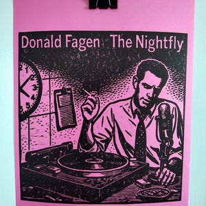 May include: A pink poster print featuring a black and white illustration of Donald Fagen, with the text "Donald Fagen The Nightfly." The image depicts a man at a turntable with a microphone, clock, and notepad.