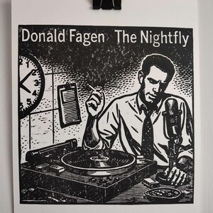May include: Black and white print of Donald Fagen's album, The Nightfly. The image features a man in a shirt and tie, smoking, with a microphone, record player, and clock. The print is held by a black binder clip.