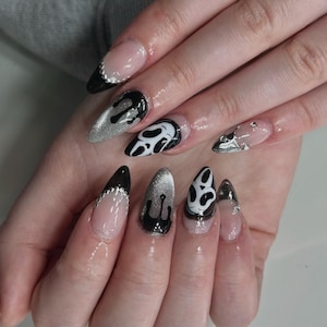 May include: A set of long, pointed fingernails with a variety of designs. Some nails are painted black with silver glitter, others have a black and white graphic design. One nail has a silver glitter drip design.