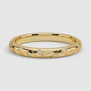 Puede incluir: Un anillo de banda de oro amarillo pulido con un patrón de enredadera grabado que envuelve toda la circunferencia. Pequeñas piedras preciosas redondas y transparentes están engastadas en las hojas del diseño, añadiendo brillo al metal.