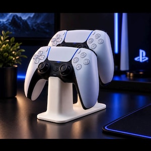Op de afbeelding: Twee draadloze gamecontrollers in wit en zwart staan op een witte oplaadstandaard. De controllers hebben een tweekleurig ontwerp met zwarte joysticks, richtingsknoppen en actiesymbolen, terwijl de oplaadbasis een gebogen steun heeft.