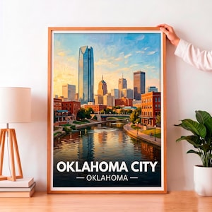 May include: A framed wall art print depicting the Oklahoma City skyline at sunset, featuring the Devon Tower, a river flowing through the city center, and brick buildings. The text OKLAHOMA CITY — OKLAHOMA is printed in white at the bottom.
