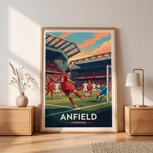 Könnte beinhalten: Ein gerahmter Kunstdruck, der ein Fußballspiel im Anfield-Stadion in Liverpool zeigt. Die Illustration zeigt einen Spieler im roten Trikot mit der Nummer 8, der den Ball aufs Tor schießt, sowie weitere Spieler in weißen und blauen Trikots auf dem Spielfeld.