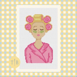 May include: A cross-stitch pattern featuring a person with blonde hair in pink hair rollers, wearing green under-eye patches and a pink robe. The design is set against a white background with a yellow and light blue checkered border and a logo.