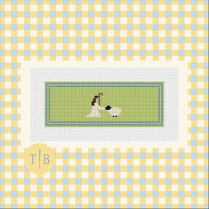 May include: A cross-stitch pattern on white fabric featuring a green rectangular border with blue trim. In the centre, a figure in a white robe holds a brown staff next to a small white sheep with black details. A logo with the letters T and B is visible.