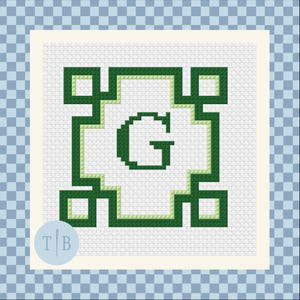 May include: A cross-stitch pattern on white fabric featuring a dark green letter G centered within a geometric border. The border consists of dark green and light green lines forming a square frame with small squares at each of the four corners.