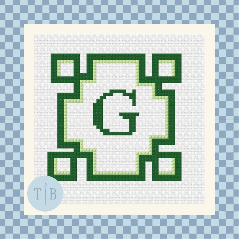 May include: A cross-stitch pattern on white fabric featuring a dark green letter G centered within a geometric border. The border consists of dark green and light green lines forming a square frame with small squares at each of the four corners.