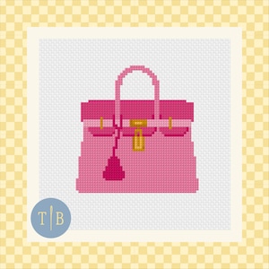 May include: A cross-stitch pattern featuring a pink handbag with a darker pink top flap, a single handle, a gold-colored central clasp, and a hanging charm. The design is set against a white grid background with a circular logo containing the letters T and B.