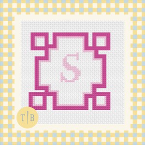May include: A cross-stitch pattern on white Aida fabric featuring a central light pink letter S enclosed within a bold, geometric magenta border. The design is framed by a yellow and light blue checkered border, with a circular logo containing T B.