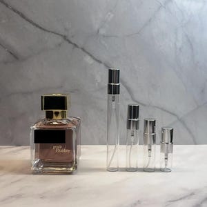 May include: A perfume bottle with a gold cap and a black label, next to four clear glass spray bottles of varying sizes. The perfume bottle has the words "gentle Fluidity" printed on it.