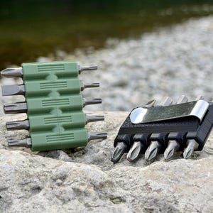 Könnte beinhalten: Zwei Sätze von Schraubendreher-Bits in rechteckigen Halterungen. Eine Halterung ist olivgrün und hält fünf Bits horizontal. Die andere ist schwarz, hält fünf Bits vertikal und verfügt über einen silbernen Metall-Taschenclip an der Seite.