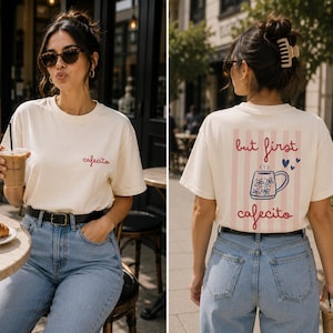 Könnte beinhalten: Ein cremefarbenes Kurzarm-T-Shirt mit dem Wort cafecito in roter Schreibschrift auf der linken Brust. Die Rückseite zeigt ein rosafarbenes Streifenrechteck mit dem Text but first cafecito in Rot und einer blauen, geblümten Tasse mit Herzen.